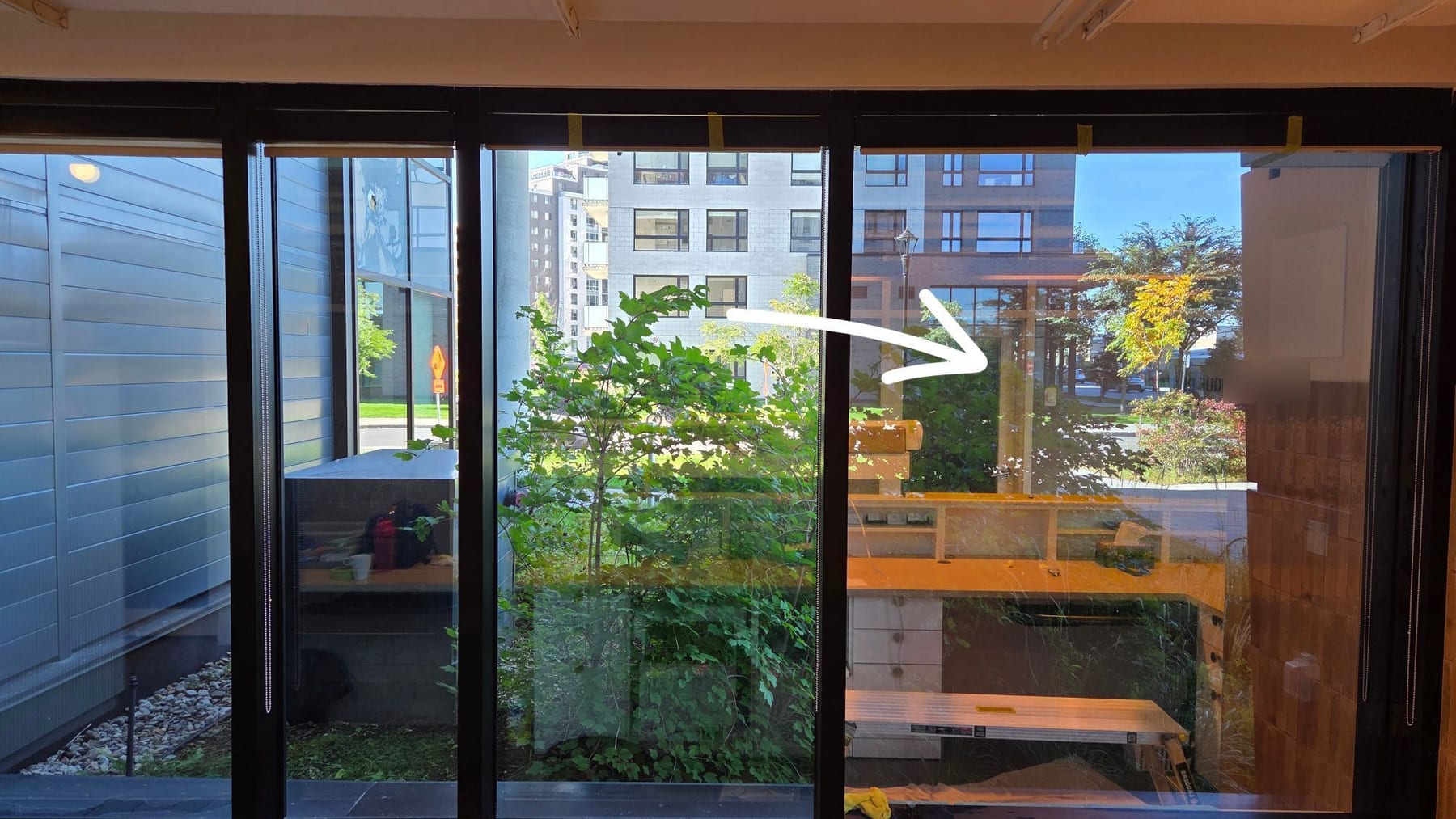 Vue de l'intérieur d'une grande fenêtre à plusieurs vitres : des vitres avec pellicule et des vitres sans pellicule côte à côte, avec une flèche blanche ajoutée sur la photo